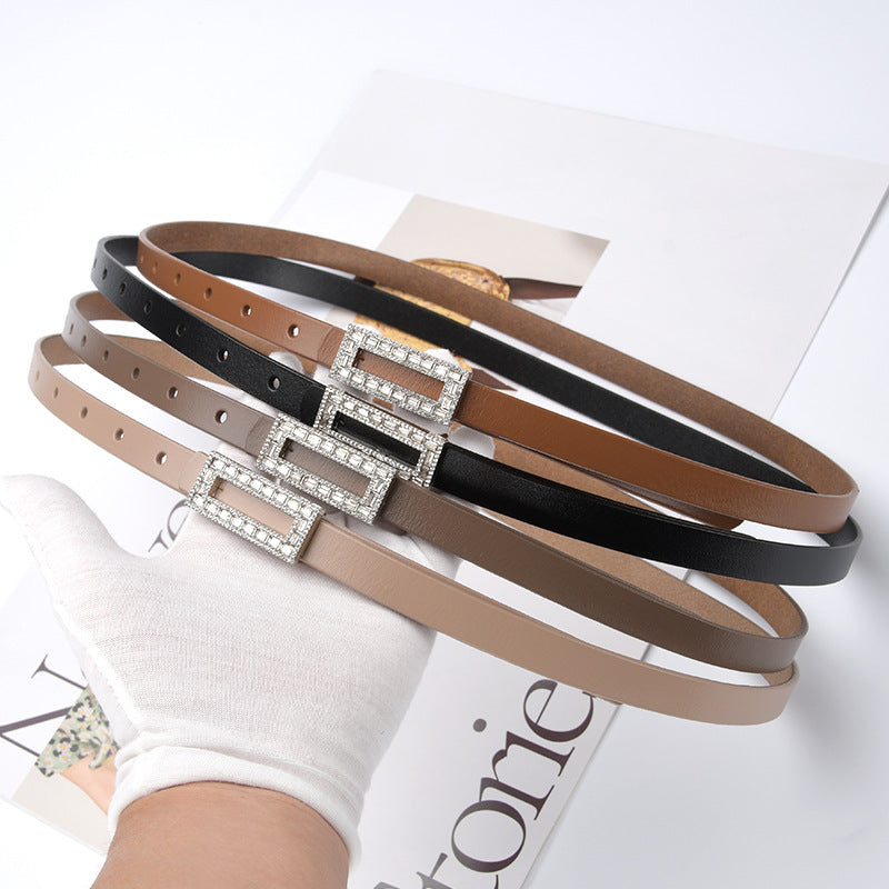 Lot de trois ceintures fines pour femme Clarisse en cuir lisse marron, noir et beige avec boucle ardillon rectangulaire ornée de strass brillants maintenues par une main gantée blanche