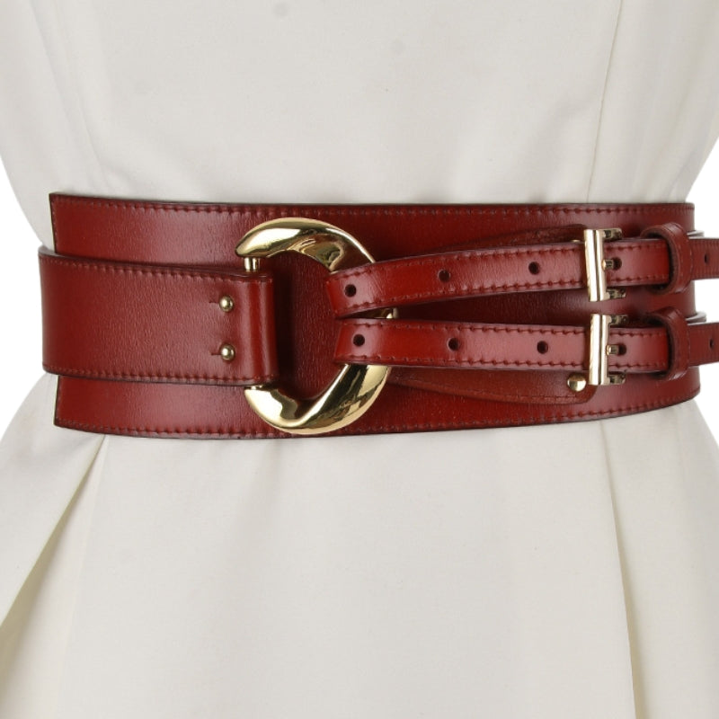 Ceinture corset large en cuir simili bordeaux avec boucle dorée et double passant, portée sur une robe blanche.