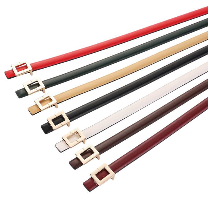 Plusieurs ceintures fines Ornement en cuir nubuck, de différentes couleurs (rouge, vert, beige, noir, blanc, marron, bordeaux), chacune avec une boucle carrée dorée minimaliste.