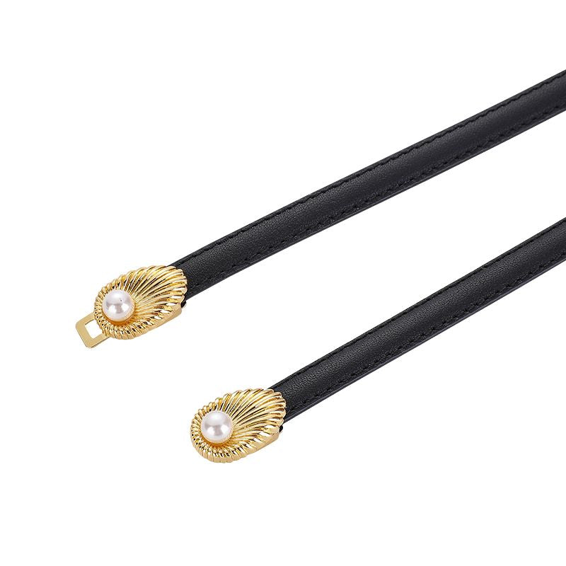Ceinture fine noire pour femme, modèle Pivoine, ornée d'une boucle décorative dorée en forme de coquillage avec une perle nacrée au centre et d'un fermoir à double crochet.
